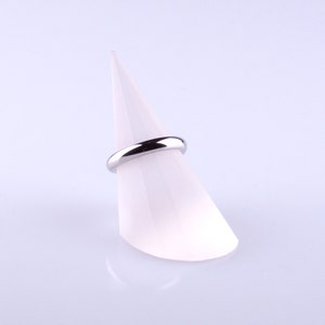 May include: A silver wedding band displayed on a white cone-shaped ring holder.