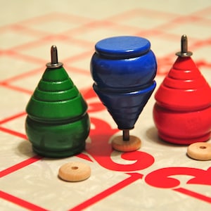 May include: Three wooden spinning tops, one green, one blue and one red, on a white and red chequered surface.