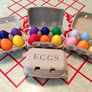 以下が含まれることがあります： カラフルにペイントされた卵が詰まった、3つの段ボール製の卵カートン。カートンには「EGGS」とラベルが貼られています。