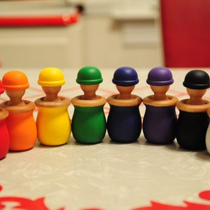 Peut inclure: Un ensemble de dix jouets d'empilage en bois colorés. Chaque jouet a une couleur différente et un petit sommet rond. Les jouets sont disposés en rangée de gauche à droite, avec le jouet rouge à gauche et le jouet blanc à droite.