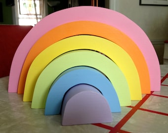 May include: A rainbow-colored wooden stacking toy with six arches in shades of pink, orange, yellow, green, blue, and purple.