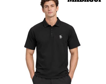 Op de afbeelding: Een zwart poloshirt met korte mouwen, een kraag, een sluiting met drie knopen en een klein zilverkleurig geborduurd logo van een persoon op een paard op de linkerborst. De tekst MADAGUI staat in het zwart in de rechterbovenhoek van de afbeelding.