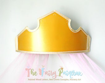 May include: A golden crown-shaped canopy with a scalloped edge and a pink tulle skirt. The crown is trimmed with a gold rope-like border. The text "The Fairy Paintbox" is printed below the crown.