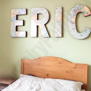 May include: A light green wall with a wooden headboard bed and a set of large letters spelling "ERIC" made from paper with a world map design.