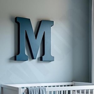 Peut inclure: Une grande lettre M en bois bleu foncé, montée sur un mur bleu clair. La lettre est tridimensionnelle et a une surface légèrement texturée.