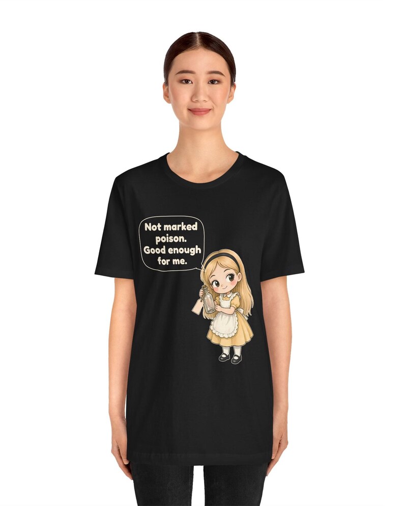 May include: A black t-shirt featuring a graphic of a blonde character in a yellow dress and white apron holding a glass bottle. A speech bubble above the character contains the text: Not marked poison. Good enough for me.