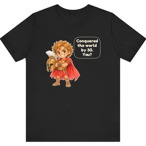 May include: A black t-shirt featuring a cartoon illustration of a warrior in golden armor and a red cape, holding a helmet. A speech bubble next to the character contains the text: Conquered the world by 30. You?