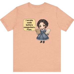 May include: A peach-colored t-shirt featuring a cartoon illustration of a person in a blue Victorian-style dress holding punch cards and papers. A yellow speech bubble contains the text: I wrote code before computers. Flex.