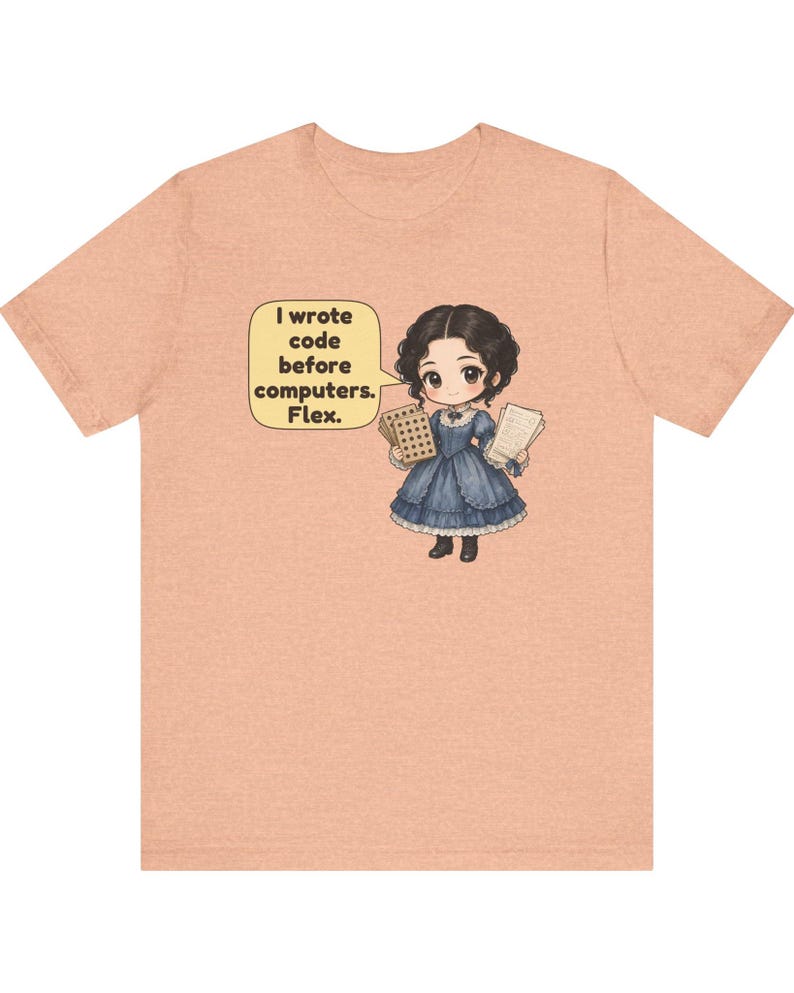 May include: A peach-colored t-shirt featuring a cartoon illustration of a person in a blue Victorian-style dress holding punch cards and papers. A yellow speech bubble contains the text: I wrote code before computers. Flex.