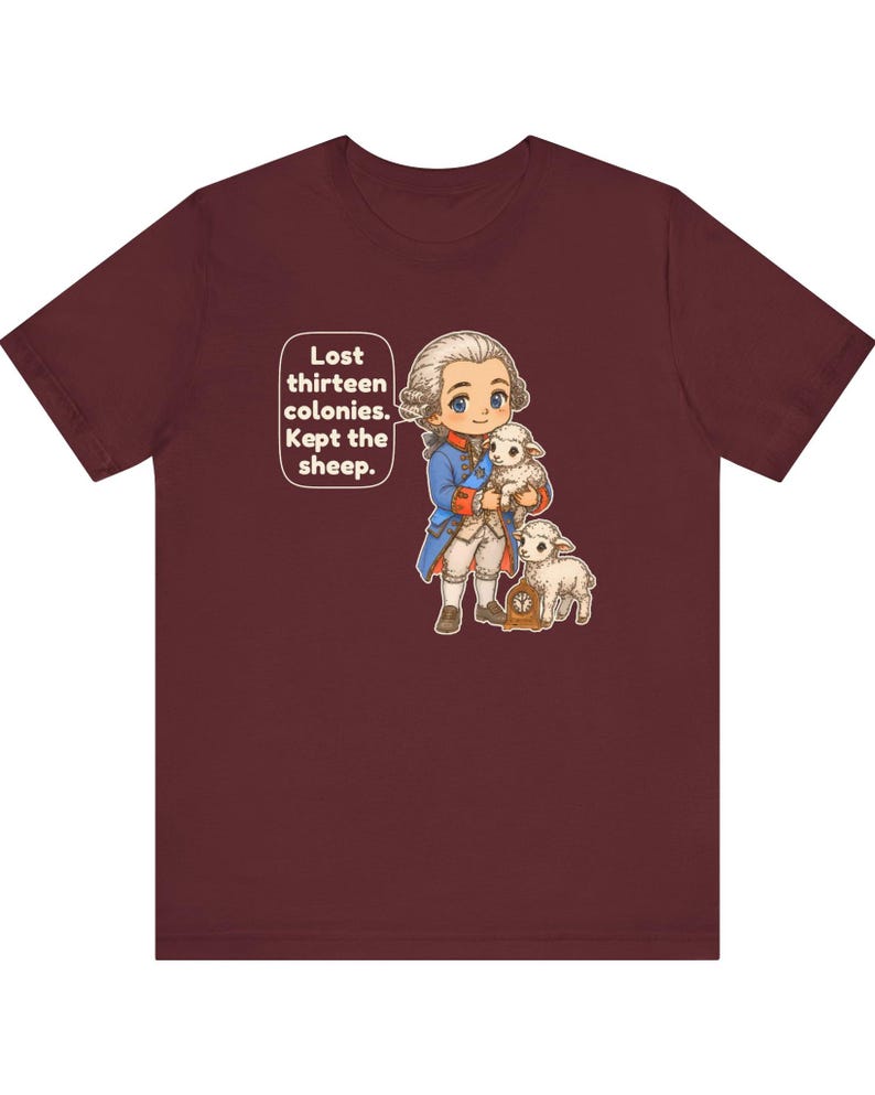 Peut inclure: Un t-shirt &agrave; manches courtes bordeaux avec une illustration de style dessin anim&eacute; repr&eacute;sentant un personnage historique en manteau bleu tenant un agneau blanc, avec un autre agneau et une petite horloge. Texte : Lost thirteen colonies. Kept the sheep.