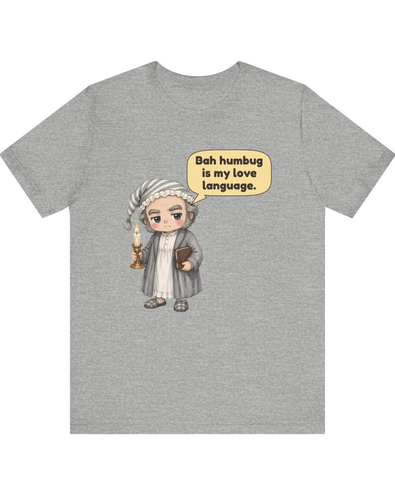 Puede incluir: Una camiseta gris jaspeado con una ilustraci&oacute;n de dibujos animados de un personaje con gorro de dormir y bata que sostiene una vela y un libro. Un globo de texto sobre el personaje contiene: Bah humbug is my love language.
