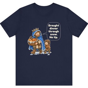 May include: A navy blue t-shirt featuring a graphic of a king in a blue cloak carrying a basket of bread, accompanied by a child. A speech bubble contains the text: Brought dinner through snow. No tip. The design is centered on the chest.