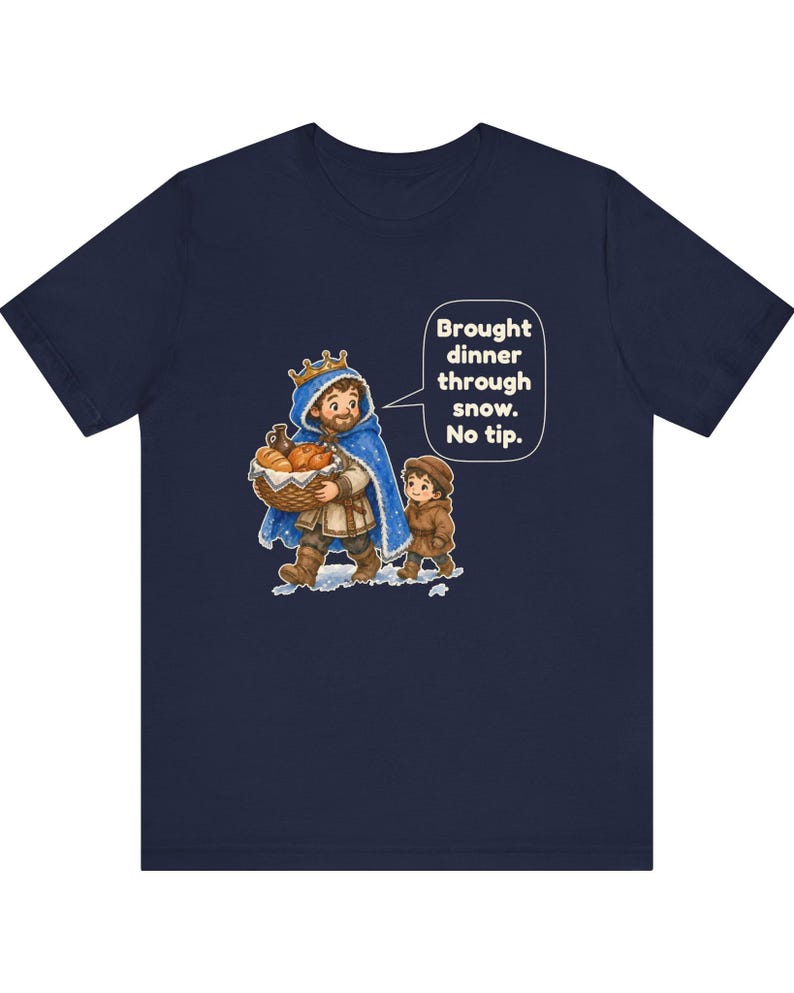 May include: A navy blue t-shirt featuring a graphic of a king in a blue cloak carrying a basket of bread, accompanied by a child. A speech bubble contains the text: Brought dinner through snow. No tip. The design is centered on the chest.