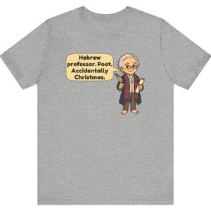 Pu&ograve; includere: Una t-shirt grigio melange con un'illustrazione a cartone animato di un professore che tiene in mano una penna e una pergamena. Un fumetto accanto al personaggio contiene il testo: Hebrew professor. Poet. Accidentally Christmas.
