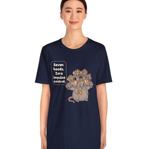 May include: A navy blue t-shirt featuring a graphic of a seven-headed rat wearing small gold crowns and holding a piece of yellow cheese. A speech bubble next to the rat contains the text: Seven heads. Zero impulse control.