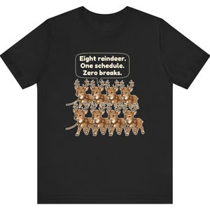 K&ouml;nnte beinhalten: Ein schwarzes kurz&auml;rmeliges T-Shirt mit einer Grafik von acht braunen Rentieren, die in zwei Reihen angeordnet sind. &Uuml;ber den Rentieren befindet sich eine wei&szlig;e Sprechblase mit dem Text: Eight reindeer. One schedule. Zero breaks.