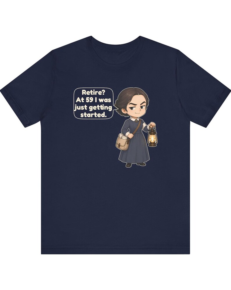 May include: A navy blue short-sleeve t-shirt featuring a cartoon illustration of a person in a dark dress carrying a satchel and a lit lantern. A speech bubble above the figure contains the text: Retire? At 59 I was just getting started.