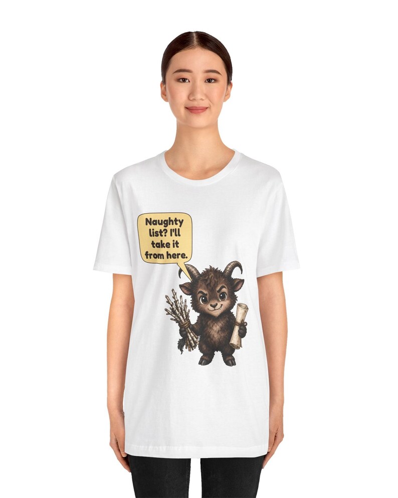 Puede incluir: Una camiseta blanca con un gr&aacute;fico de una peque&ntilde;a criatura marr&oacute;n con cuernos que sostiene un manojo de palos y un pergamino. Un globo de texto amarillo sobre la criatura contiene el texto: Naughty list? I'll take it from here.