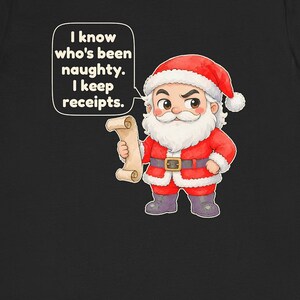 May include: A black t-shirt featuring a cartoon Santa Claus with a white beard, red suit, and hat. Santa holds a scroll and has a speech bubble with the text: I know who's been naughty. I keep receipts. The design is centered on the shirt.