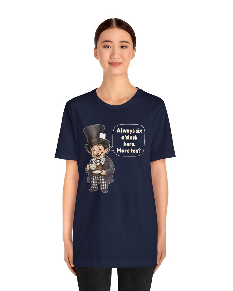 May include: A navy blue t-shirt featuring a graphic of a character wearing a tall top hat, a polka dot bow tie, and a suit, holding a teacup and saucer. Next to the character is a speech bubble with the text: Always six o'clock here. More tea?