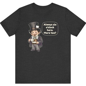 May include: A dark heather gray t-shirt featuring a graphic of a character wearing a top hat, a brown vest, and checkered pants, holding a teacup. A speech bubble next to the character contains the text: Always six o'clock here. More tea?