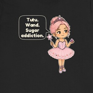 May include: A black t-shirt featuring a cartoon ballerina with pink hair, a tiara, and a pink tutu. The character holds a star-tipped wand and a small cluster of purple candies. A speech bubble contains the text: Tutu. Wand. Sugar addiction.