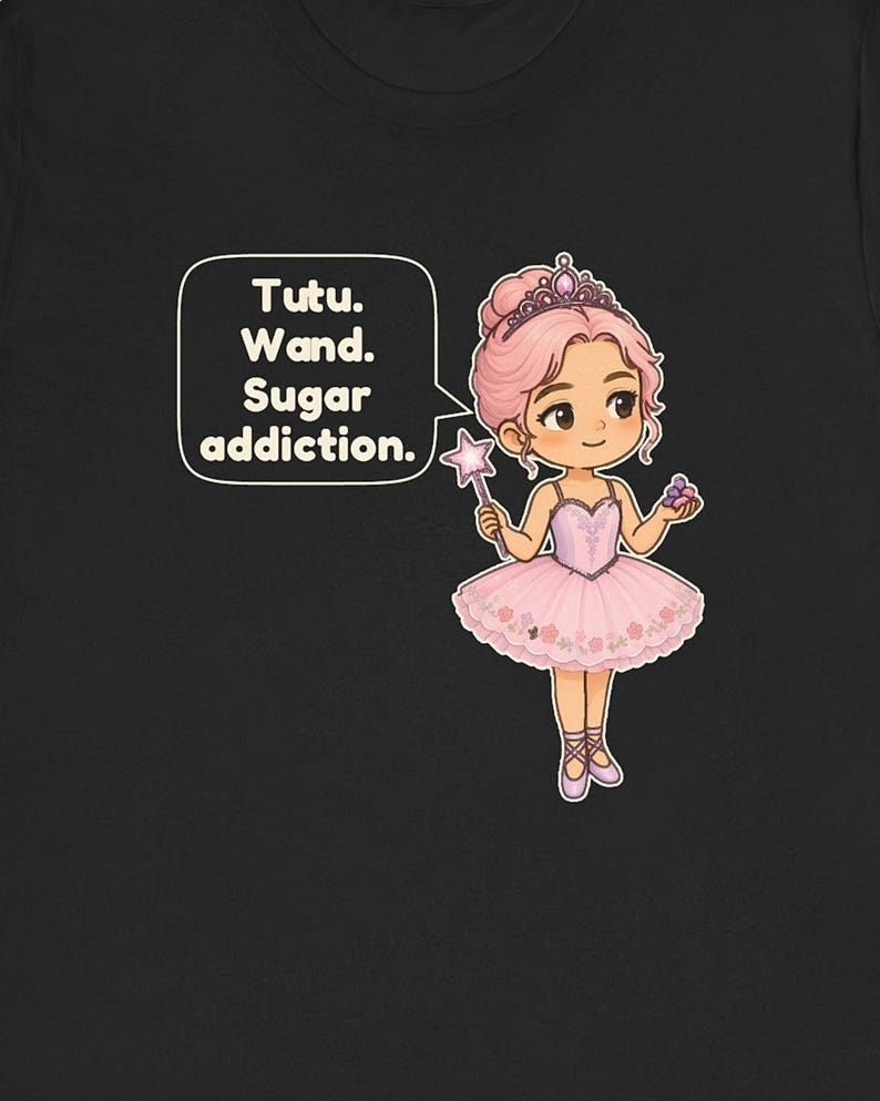 May include: A black t-shirt featuring a cartoon ballerina with pink hair, a tiara, and a pink tutu. The character holds a star-tipped wand and a small cluster of purple candies. A speech bubble contains the text: Tutu. Wand. Sugar addiction.