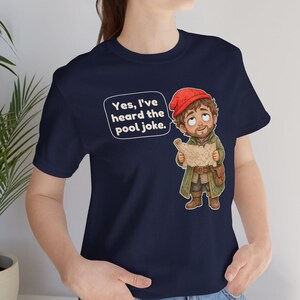 May include: A navy blue t-shirt featuring a cartoon illustration of a bearded character wearing a red cap and green coat, holding a map. A speech bubble above the character contains the text: Yes, I've heard the pool joke.