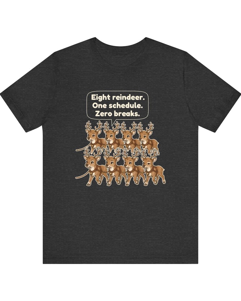 K&ouml;nnte beinhalten: Ein dunkelgraues T-Shirt mit einer Grafik von acht Cartoon-Rentieren, die in zwei Reihen angeordnet sind. &Uuml;ber den Rentieren befindet sich eine wei&szlig;e Sprechblase mit dem Text: Eight reindeer. One schedule. Zero breaks. Die Rentiere sind braun mit beigen Geweihen und Geschirren.