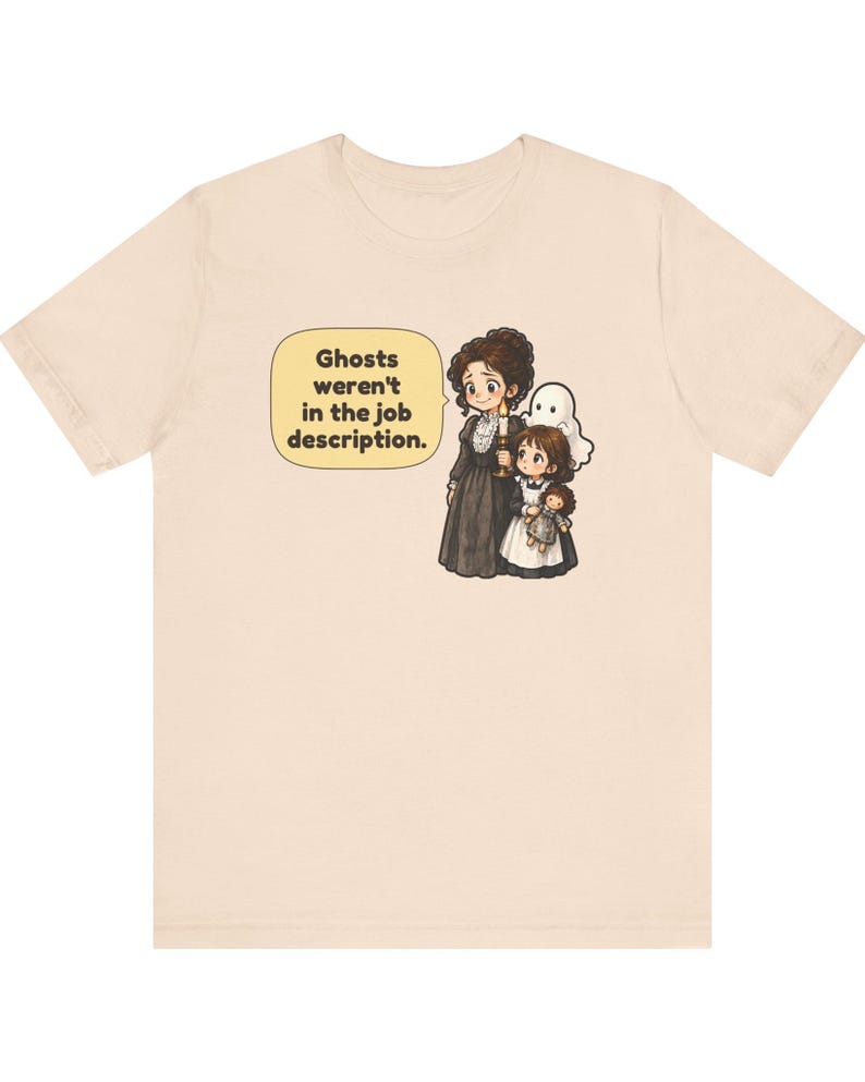 Op de afbeelding: Een lichtbeige t-shirt met een afbeelding van een persoon in een donkere jurk met een kaars, een kind met een pop en een klein wit spookje. Een tekstballon bevat de tekst: Ghosts weren't in the job description.