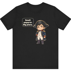 May include: A black t-shirt featuring a cartoon illustration of a historical figure in a blue military uniform with gold accents and a bicorne hat. A speech bubble next to the character contains the text: Small emperor. Big plans.