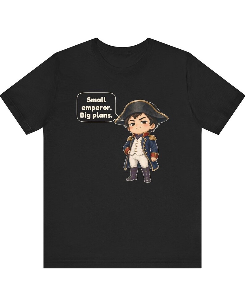 May include: A black t-shirt featuring a cartoon illustration of a historical figure in a blue military uniform with gold accents and a bicorne hat. A speech bubble next to the character contains the text: Small emperor. Big plans.