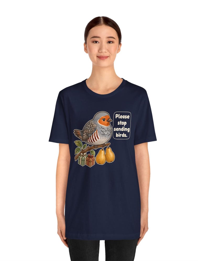 K&ouml;nnte beinhalten: Ein dunkelblaues Kurzarm-T-Shirt mit einer Grafik eines grauen und orangefarbenen Vogels, der auf einem Ast mit zwei Birnen und zwei kleinen Geschenkkartons sitzt. Eine Sprechblase neben dem Vogel enth&auml;lt den Text, Please stop sending birds.