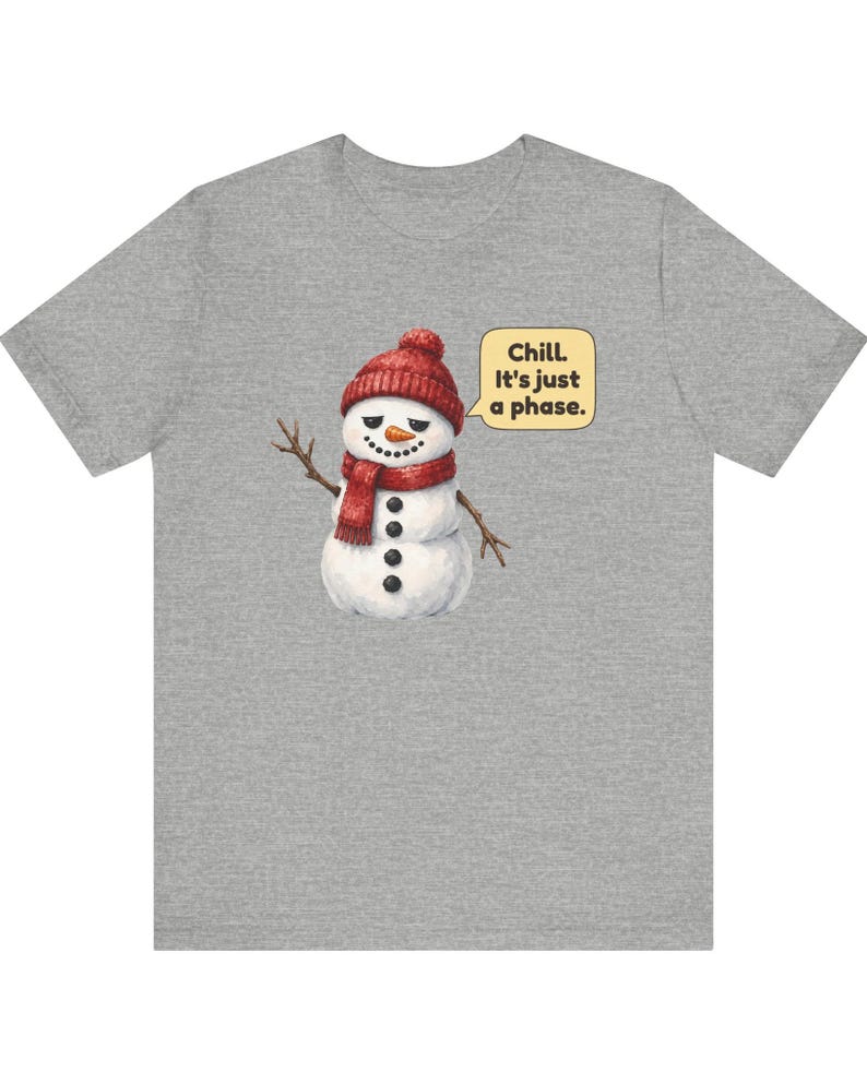 Pode incluir: Uma t-shirt cinzenta mesclada com um gr&aacute;fico de um boneco de neve a usar um gorro e um cachecol de malha vermelha. O boneco de neve tem um nariz de cenoura, bra&ccedil;os de pau e bot&otilde;es pretos. Um bal&atilde;o de fala cont&eacute;m o texto, Chill. It's just a phase.