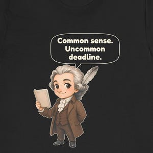 May include: A black t-shirt featuring a cartoon illustration of a historical figure with a powdered wig and a quill pen, holding a book. Above the figure is a speech bubble containing the text: Common sense. Uncommon deadline.