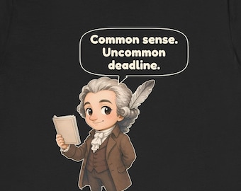 May include: A black t-shirt featuring a cartoon illustration of a historical figure with a powdered wig and a quill pen, holding a book. Above the figure is a speech bubble containing the text: Common sense. Uncommon deadline.