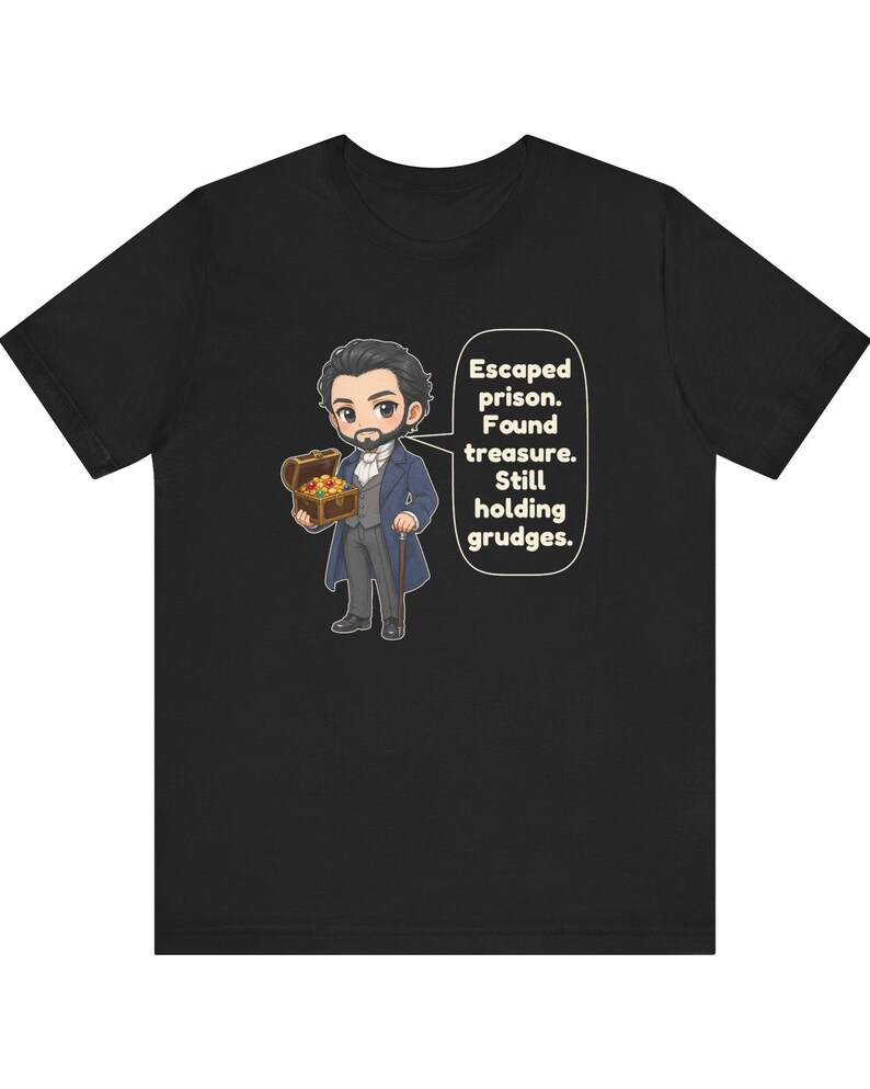 May include: A black t-shirt featuring a cartoon illustration of a bearded man in a blue coat holding a treasure chest. A speech bubble next to the character contains the text: Escaped prison. Found treasure. Still holding grudges.