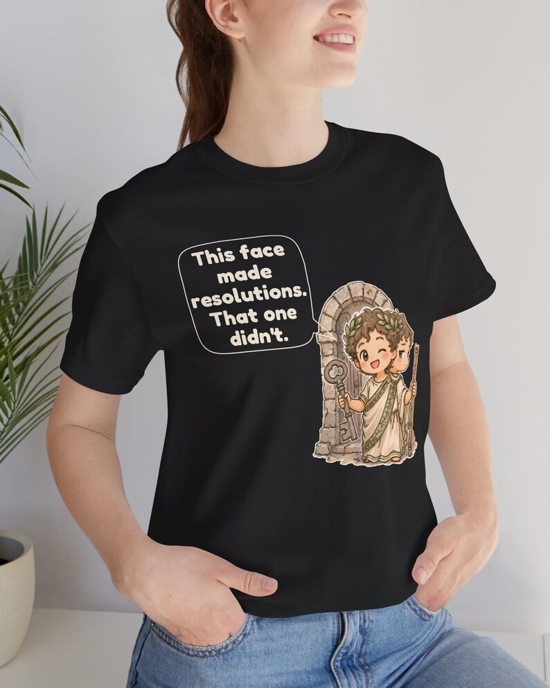 K&ouml;nnte beinhalten: Ein schwarzes T-Shirt mit einer Grafik einer zweigesichtigen r&ouml;mischen Gottheit mit Lorbeerkranz vor einem Steinbogen. Die Figur h&auml;lt einen Schl&uuml;ssel und einen Stab. Eine Sprechblase enth&auml;lt den Text: This face made resolutions. That one didn't.