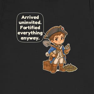 May include: A black t-shirt featuring a cartoon character in a blue and white colonial-style uniform with a tricorn hat, holding a shovel and compass. Next to the character is a wooden chest and a small fort. Text reads: Arrived uninvited. Fortified everything anyway.