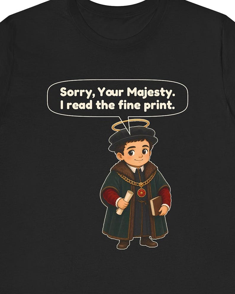 May include: A black t-shirt featuring a cartoon illustration of a person dressed in historical royal attire with a halo, holding a scroll and a book. Above the figure, a speech bubble contains the text: Sorry, Your Majesty. I read the fine print.