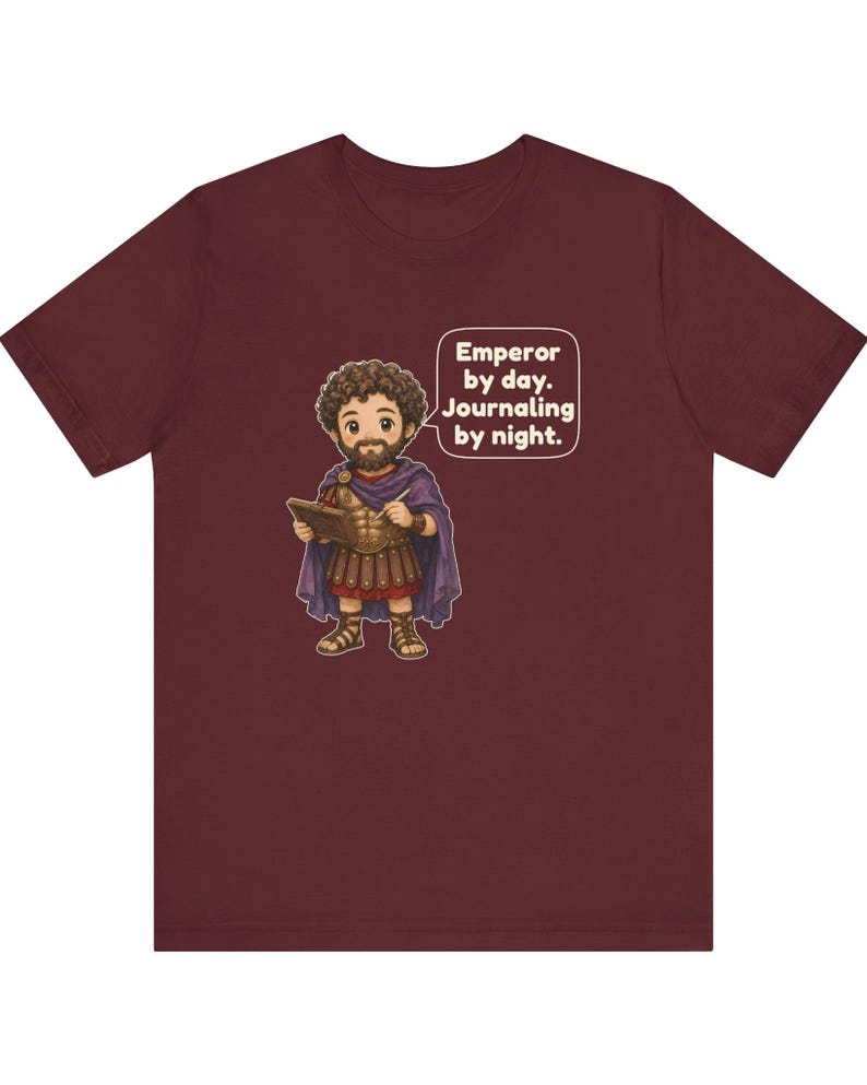 K&ouml;nnte beinhalten: Ein kastanienbraunes T-Shirt mit einer Cartoon-Illustration eines b&auml;rtigen Mannes in r&ouml;mischer R&uuml;stung und einem violetten Umhang, der ein Tagebuch und einen Stift h&auml;lt. Eine Sprechblase neben der Figur enth&auml;lt den Text: Emperor by day. Journaling by night.
