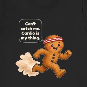 May include: A black t-shirt featuring a cartoon gingerbread person running with a red and white striped headband. A speech bubble contains the text: Can't catch me. Cardio is my thing. The gingerbread person has three dark buttons and pink cheeks.