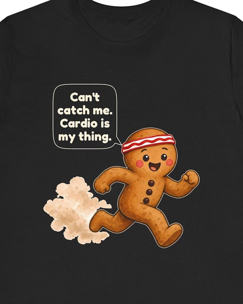 May include: A black t-shirt featuring a cartoon gingerbread person running with a red and white striped headband. A speech bubble contains the text: Can't catch me. Cardio is my thing. The gingerbread person has three dark buttons and pink cheeks.