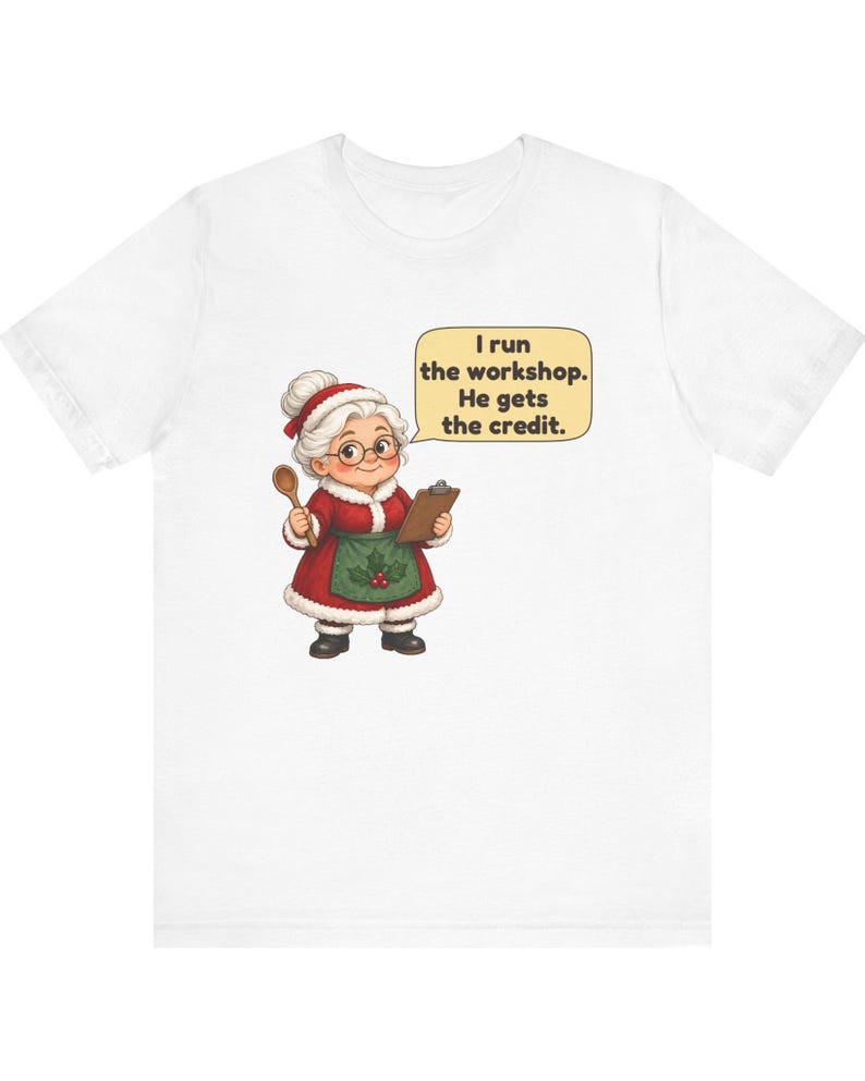 K&ouml;nnte beinhalten: Ein wei&szlig;es T-Shirt mit einer Grafik einer Figur mit wei&szlig;em Dutt, rotem Mantel mit wei&szlig;em Pelzbesatz, gr&uuml;ner Sch&uuml;rze mit Stechpalme und Brille. Die Figur h&auml;lt einen Holzl&ouml;ffel und ein Klemmbrett mit dem Text: I run the workshop. He gets the credit.