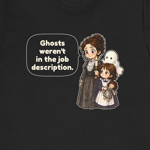May include: A black t-shirt featuring a graphic of a person in a dark dress holding a candle, a child holding a doll, and a small white ghost. A speech bubble contains the text: Ghosts weren't in the job description.