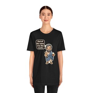 Peut inclure: Un t-shirt noir avec une illustration de dessin anim&eacute; repr&eacute;sentant un homme barbu en toge bleue tenant un parchemin et un bol. Une bulle au-dessus du personnage contient le texte : Out of the cave. Into the snacks. Le motif est centr&eacute;.
