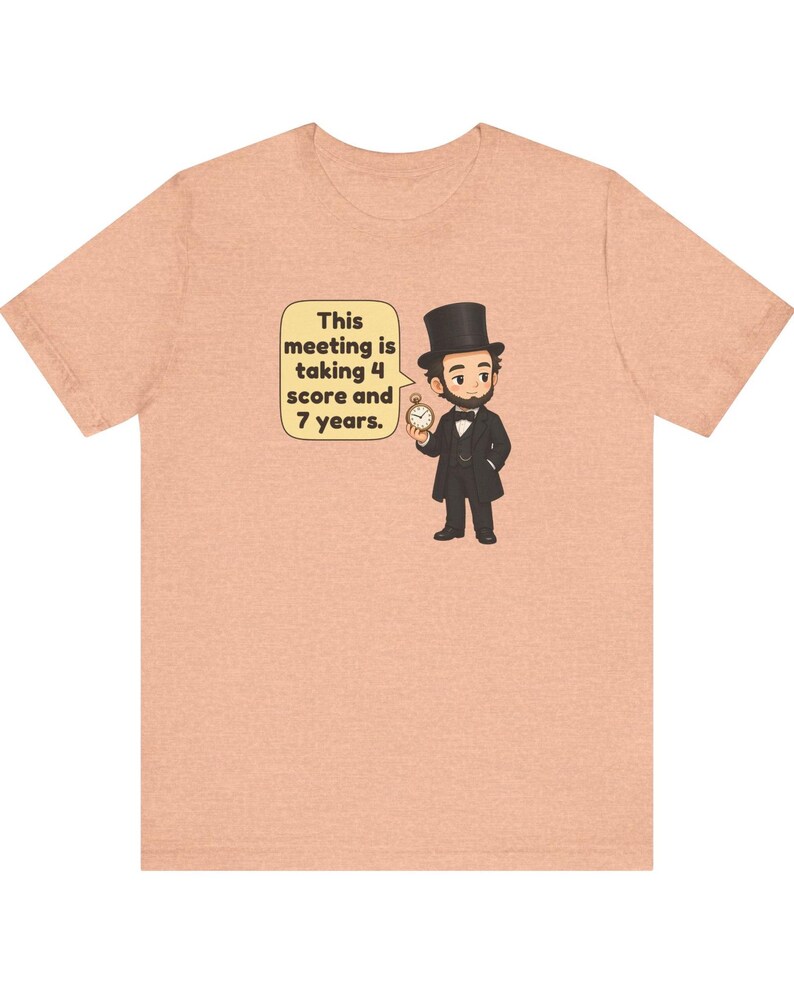 May include: A peach-colored t-shirt featuring a cartoon illustration of Abraham Lincoln in a black suit and top hat, holding a pocket watch. A speech bubble next to him contains the text: This meeting is taking 4 score and 7 years.