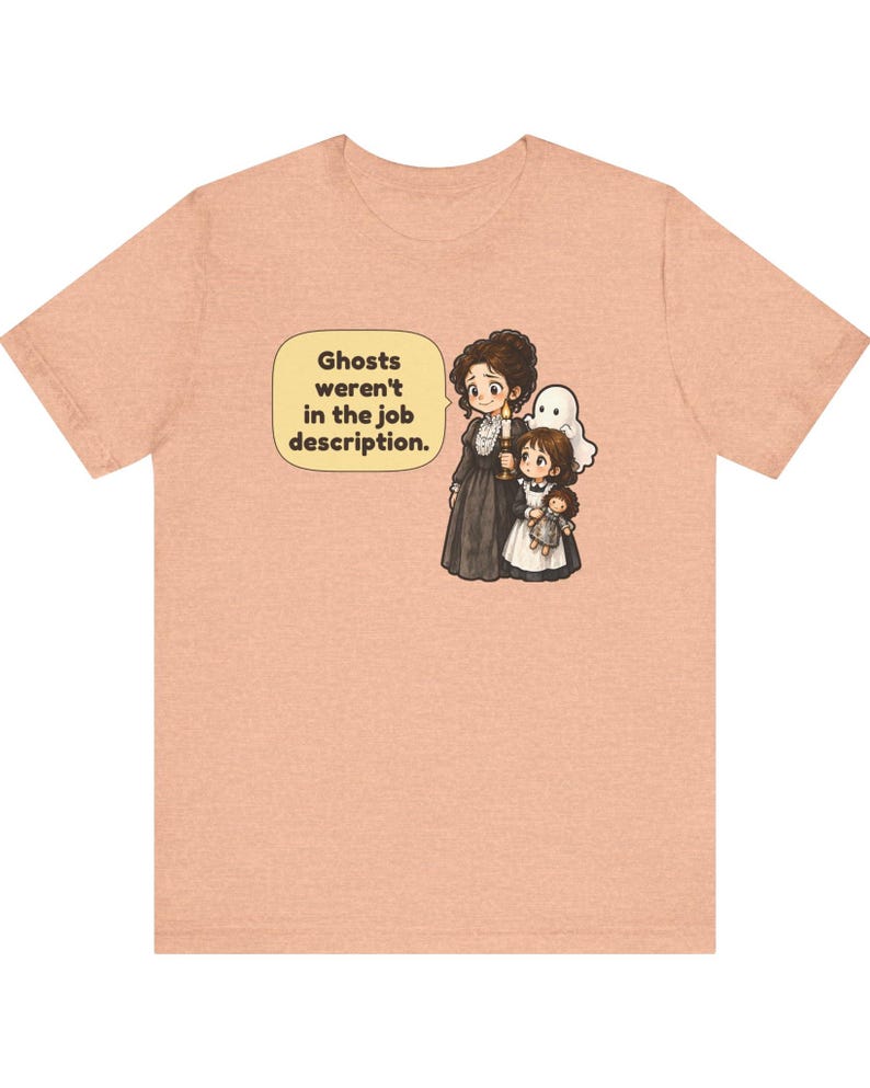 Op de afbeelding: Een perzikkleurig T-shirt met korte mouwen en een afbeelding van een persoon in een donkere jurk met een kaars, een kind met een pop en een klein wit spookje. Een tekstballon bevat de tekst: Ghosts weren't in the job description.