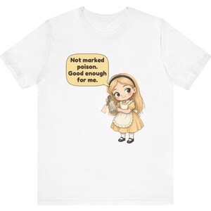 May include: A white short-sleeved t-shirt featuring a graphic of a blonde character in a yellow dress and white apron holding a small glass bottle. A speech bubble above the character contains the text: Not marked poison. Good enough for me.