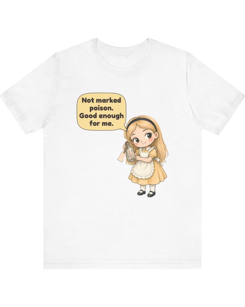 May include: A white short-sleeved t-shirt featuring a graphic of a blonde character in a yellow dress and white apron holding a small glass bottle. A speech bubble above the character contains the text: Not marked poison. Good enough for me.